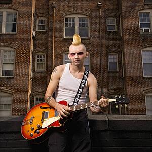 Portrait of male punk playing guitar with building in background