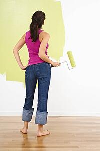 Woman standing holding paint roller admiring partially painted interior wall
