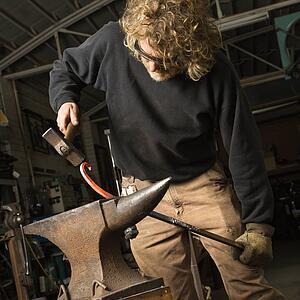 Metalsmith shaping metal on anvil