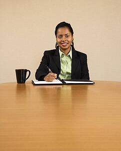 Businesswoman sitting at conference table smiling and writing in notebook
