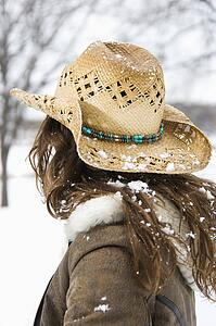 Back view of brunette woman with long hair wearing straw cowboy hat outdoors