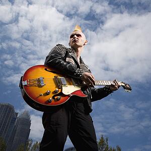 Portrait of male punk holding guitar with skyline in background