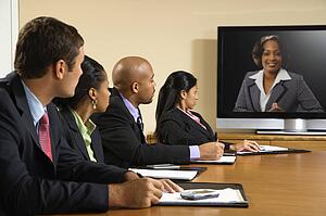 Businesspeople sitting at conference table looking at flat screen display.