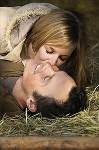 Young adult woman kissing boyfriend while lying in hay