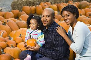 Parents and daughter picking out pumpkin and smiling at outdoor market.