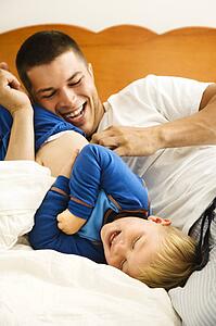 Caucasian toddler boy and father playing and tickling in bed.