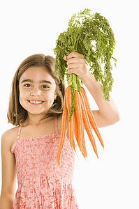 Smiling girl holding bunch of carrots against background.