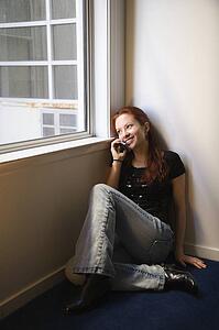 Pretty redhead young woman sitting on floor indoors by window holding cellphone to ear smiling