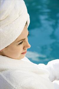 Woman wearing robe and towel on head sitting next to pool