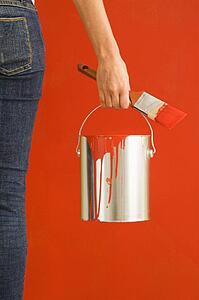 Female hand and leg holding paint can and paintbrush