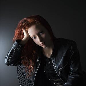 Portrait of pretty redhead young woman sitting in chair resting head on hand