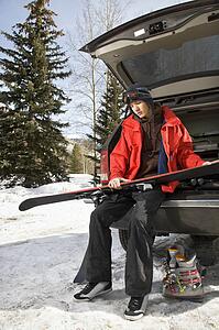 Caucasian male teenager sitting on back of SUV holding skis.