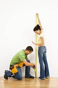 Couple measuring interior wall and smiling.
