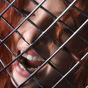 Pretty redhead young woman face with mouth open behind metal pattern