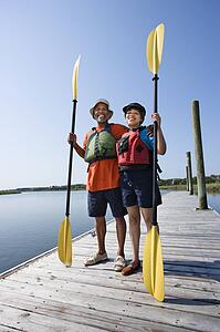 Middle-aged couple standing on dock holding paddles and smiling at viewer