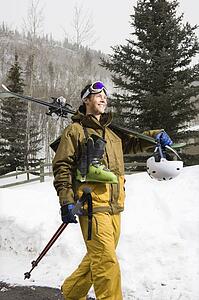 Man in winter clothing walking in snow carrying ski equipment