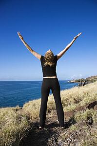 Back view of mid-adult woman standing on Maui, Hawaii coast with arms outstretched and head thrown back