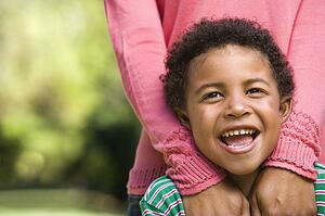 Boy smiling with mother standing behind him with hands on shoulders
