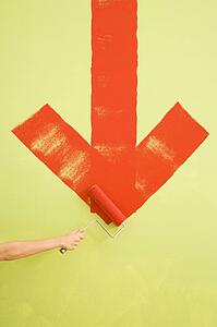 Female hand painting red downwards arrow on wall