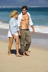 Attractive couple holding hands walking on beach smiling at eachother in Maui, Hawaii.