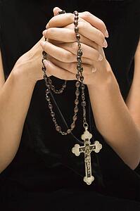 Woman holding rosary with hands clasped together
