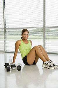 Mid adult woman sitting on floor with dumbbells smiling at viewer.