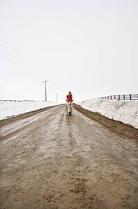 Young woman in winter clothes walking alone down muddy dirt road with snow on edges of road