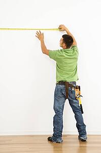 Man wearing tool belt measuring interior wall