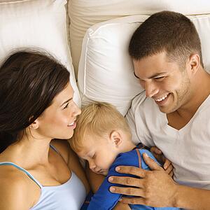 Caucasian mid adult parents with toddler son sleeping in bed. 