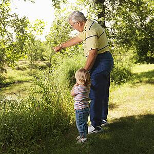 Grandfather holding granddaughter's hand by creek and pointing