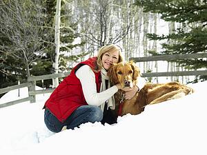 Woman hugging dog and smiling in snow covered Colorado landscape.