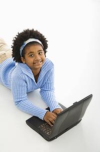 High angle view of girl laying on floor using laptop and looking up at viewer