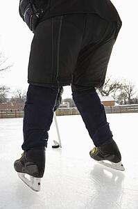 Boy in ice hockey uniform skating on ice rink moving puck.