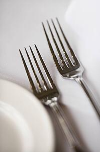 Salad fork and dinner fork with plate on white table cloth.