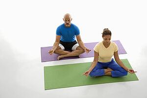 Mid adult man and woman sitting in lotus position on exercise mats with eyes closed and legs crossed.