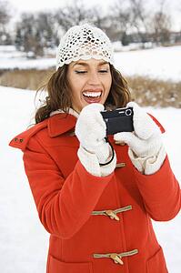 Smiling young adult female in winter clothing using digital camera outdoors