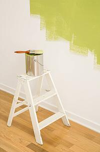 Paintbrush on can on top of step ladder with painted wall.