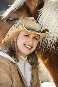 Young woman wearing cowboy hat and smiling at viewer next to horse