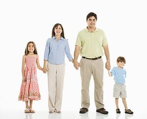 Hispanic family of four standing against white background holding hands.