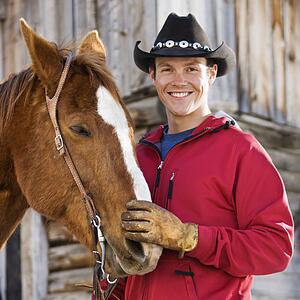 Young Caucasian man in cowboy hat petting his horse.