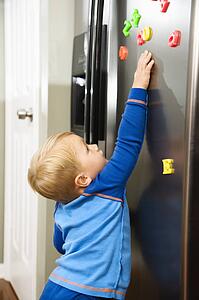 Caucasian toddler boy reaching for magnets on refrigerator.