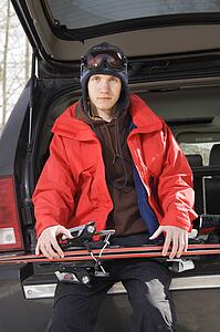 Male teen sitting on back of SUV holding skis