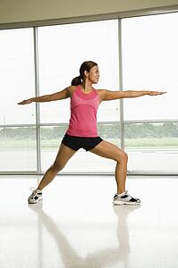 Mid adult woman standing in yoga warrior pose smiling.