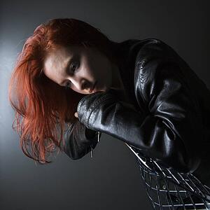 Pretty redhead young woman wearing leather jacket hanging over back of chair