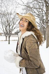 Female smiling at viewer while holding snowball and wearing straw cowboy hat.
