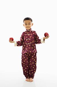 Boy in traditional attire standing with red apple in each hand.