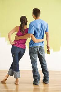 Couple standing in front of partially painted wall with arms around each other.