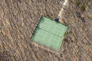 Aerial view of tennis court in bare wooded area.