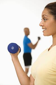Woman exercising using dumbbells with man in background