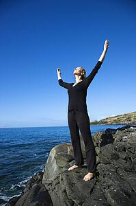 Caucasian mid-adult woman standing on rocky coast of Maui, Hawaii with arms outstretched.